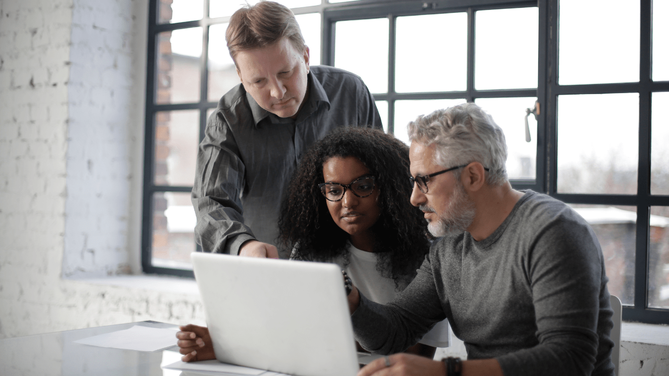 Three colleagues working together around a laptop